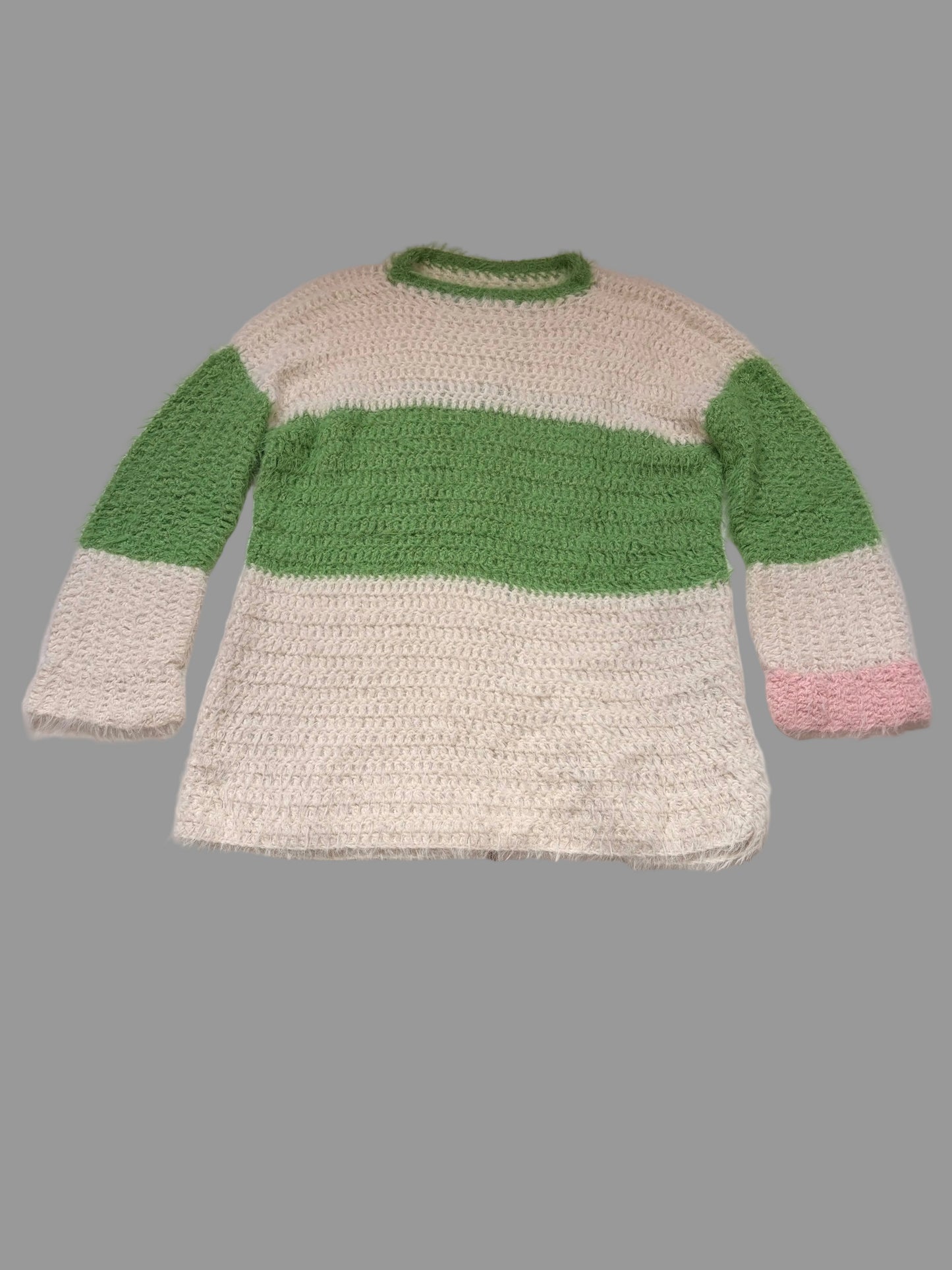 A fuzzy crochet jumper sweater with a cream body, a wide green horizontal stripe across the chest, green sleeves, and a small pink accent on the cuff, laid flat on a white table.