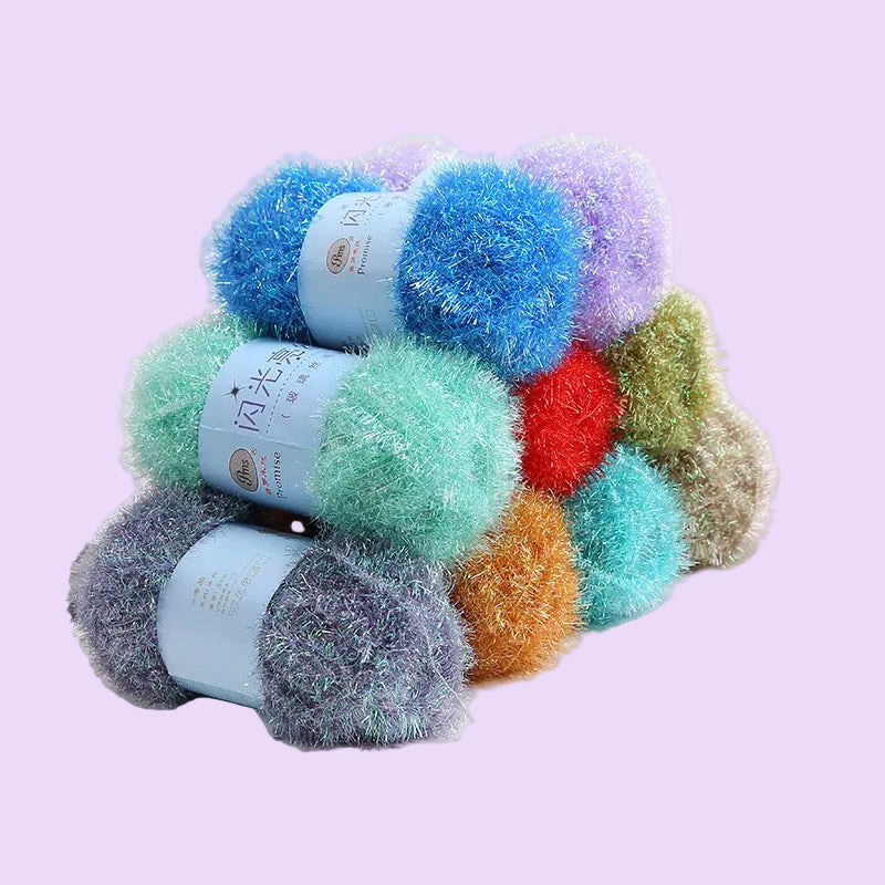 Four balls of fluffy, shimmery yarn in assorted colors including blue, mint green, lavender, red, orange, and gray, stacked together on a white surface with a small decorative rose in the background.