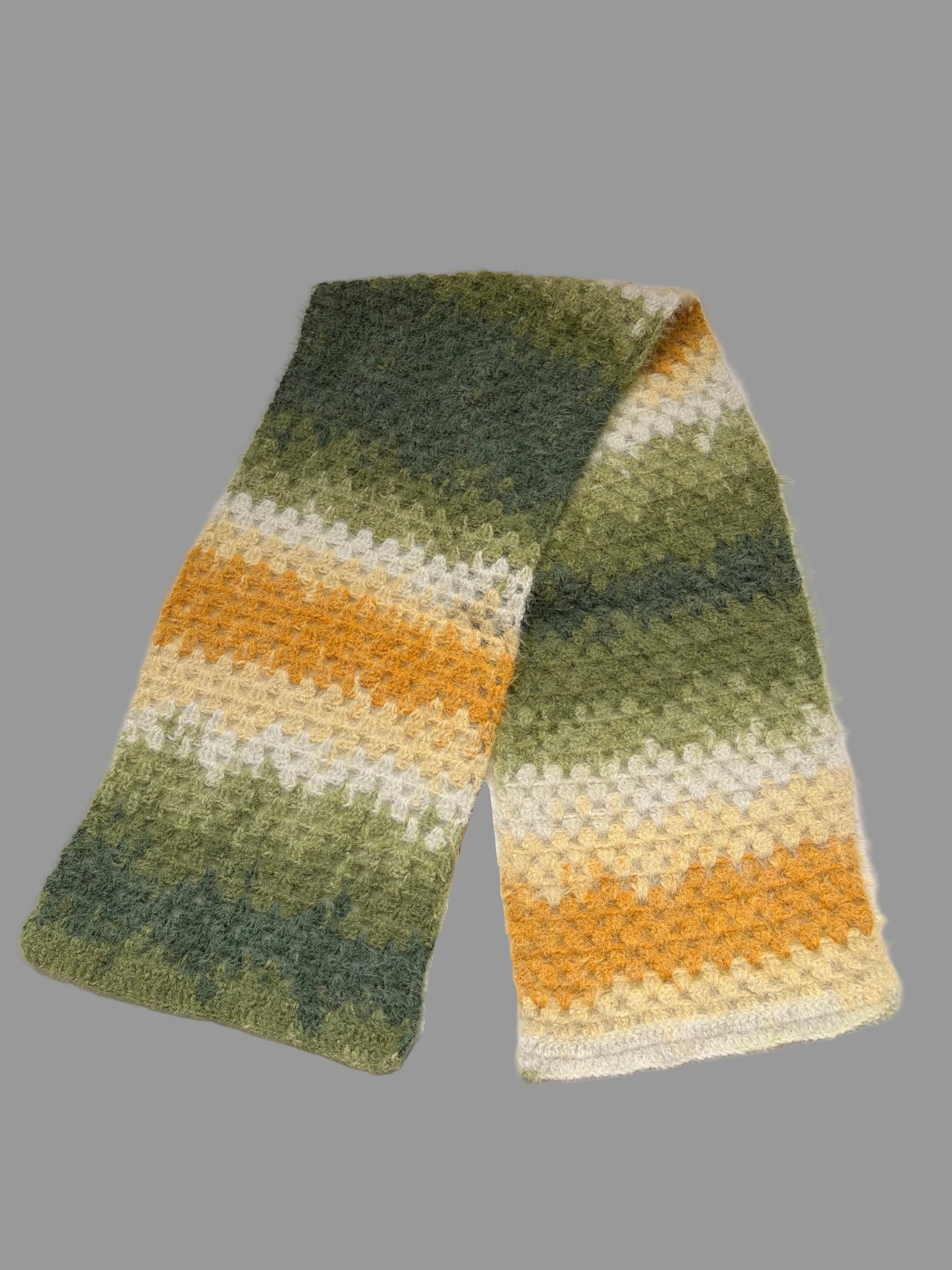 A fuzzy crochet scarf with a striped pattern in shades of green, yellow, and cream, laid flat on a white surface.