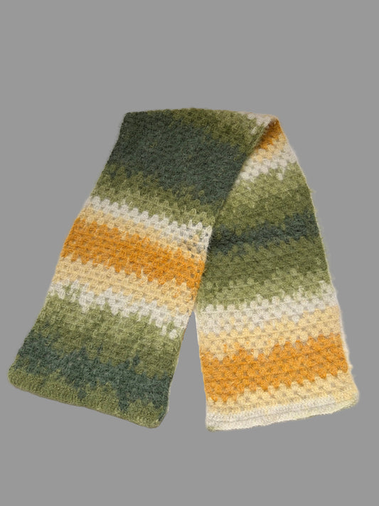 A fuzzy crochet scarf with a striped pattern in shades of green, yellow, and cream, laid flat on a white surface.