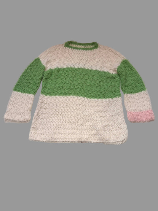 A fuzzy crochet jumper sweater with a cream body, a wide green horizontal stripe across the chest, green sleeves, and a small pink accent on the cuff, laid flat on a white table.