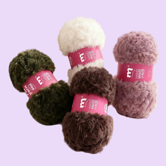 Four fluffy yarn skeins in olive green, cream, brown, and dusty mauve, each wrapped with a pink label, arranged on a white surface with soft window blinds in the background. Chinese promotional text appears at the top.