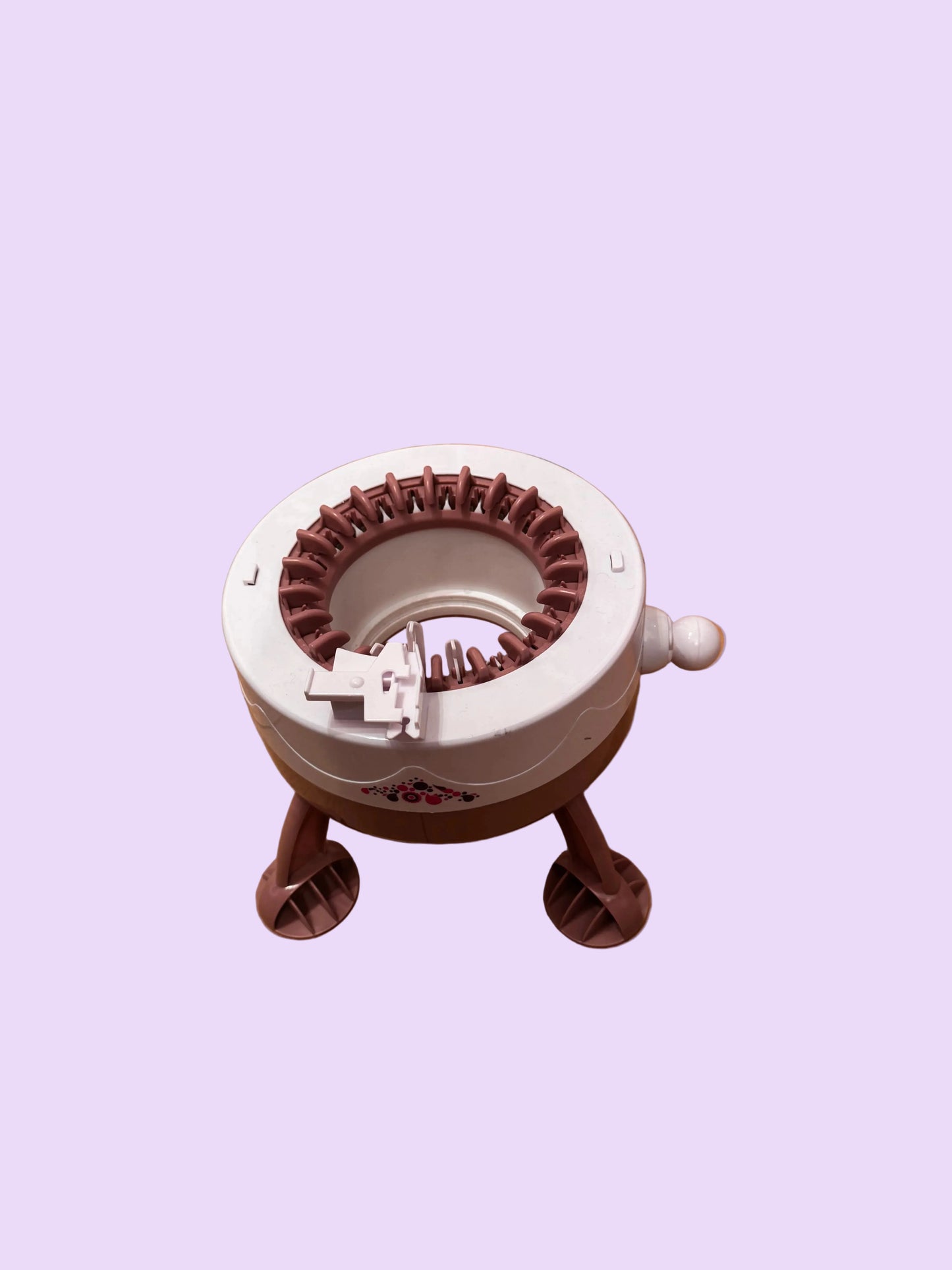 A small circular knitting loom machine with a white top and brown legs, placed on a wooden floor.